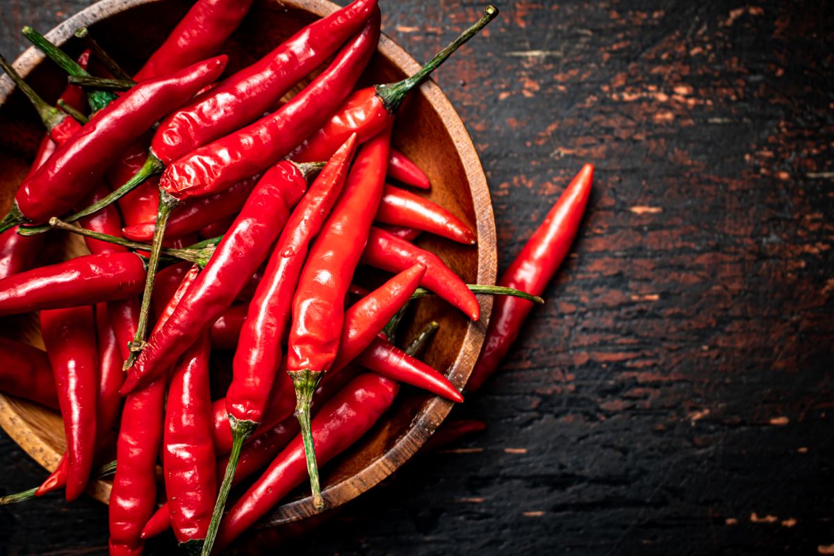 Wooden plate with hot chili peppers. On a rustic dark background.