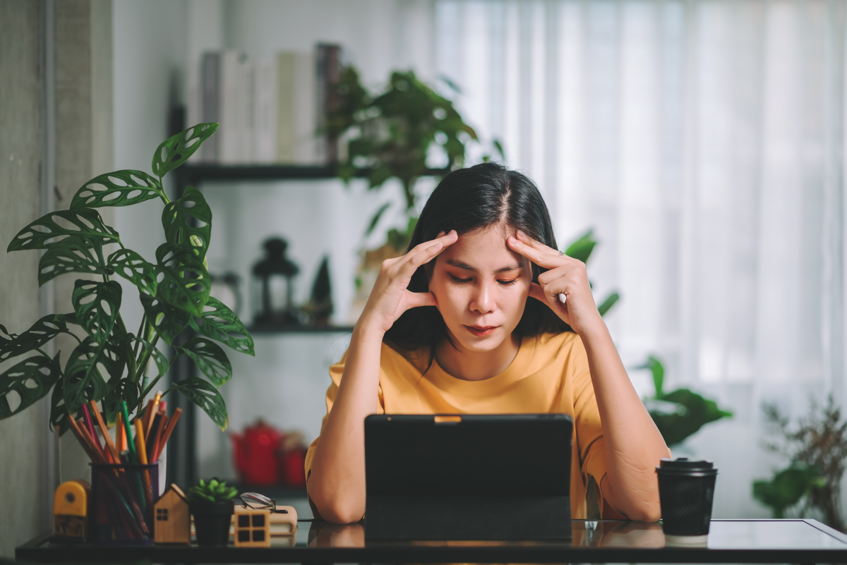 Asian woman freelancer wearing yellow t-shirt have headache from stress and office syndrome symptom, work at home, Mental health and work life balance concept.