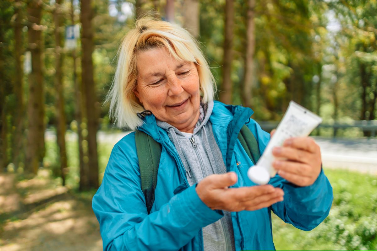 Blonde 50s 60s woman applying sunscreen lotion while traveling in the mountains 